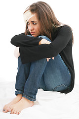 Image showing Sad girl teenager sits twining arms about legs. Isolated on a wh