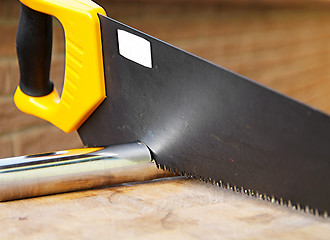 Image showing Wooden saw used for cutting a metal pipe