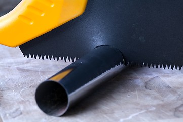 Image showing Wooden saw used for cutting a metal pipe