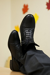 Image showing Black leather shoes crossed on table