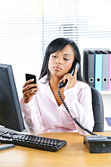 Image showing Black businesswoman using two phones at desk