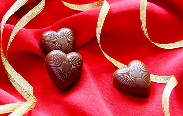 Image showing Chocolate hearts and gold ribbon on a red background.