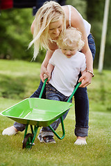 Image showing Mother helping her kid in pushing wheelbarrow