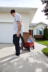 Image showing Father Pulling Son Sitting in Wagon