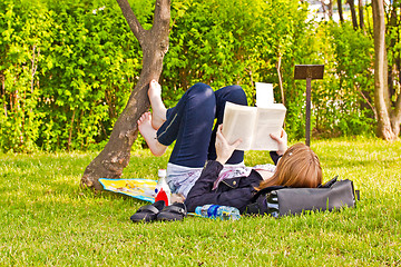 Image showing Young girl with a book lying on a lawn in a park