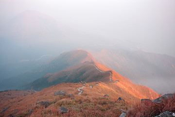 Image showing dark landscape with fog between hills and orange sky before sunr