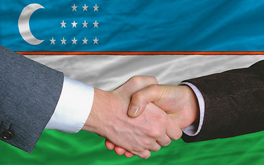 Image showing businessmen handshake after good deal in front of uzbekistan fla