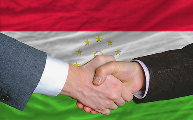 Image showing businessmen handshake after good deal in front of tajikistan fla