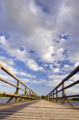 Image showing Long wooden plank bridge over lake and cloudy sky.