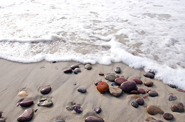 Image showing Sea waves beat stones lying in sand on coast line.