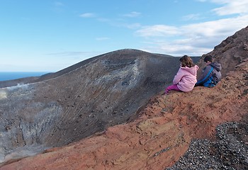 Image showing Girl and boy sitting on the rim of volcano crater of Vulcano island near Sicily, Italy