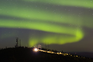 Image showing Aurora Borealis over hill with antennas and car with lights on