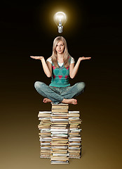 Image showing woman in lotus pose balancing on pile of books and bulb