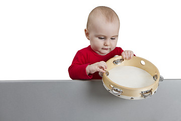 Image showing young child holding tambourine behind grey shield