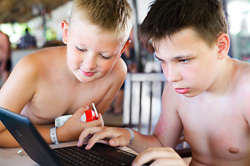 Image showing Two boys play a laptop on rest in a bar on a beach