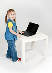 Image showing little girl in blue jeans standing at a table with a laptop