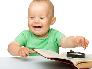 Image showing Little child play with book and magnifier