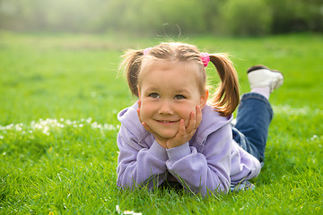 Image showing Little girl is laying on green meadow