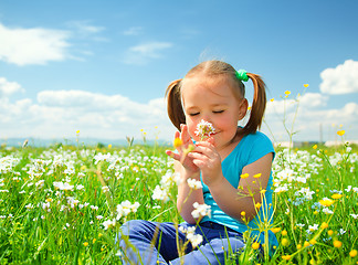 Image showing Little girl is smelling flowers on green meadow