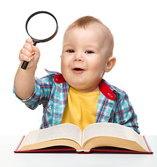 Image showing Little child play with book and magnifier