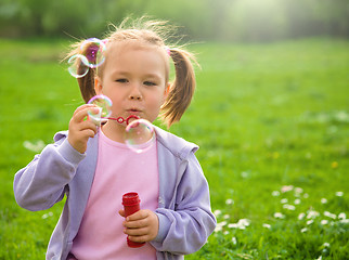 Image showing Little girl blows soap bubbles on meadow