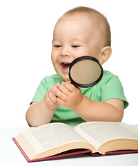 Image showing Little child play with book and magnifier