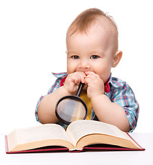 Image showing Little child play with book and magnifier