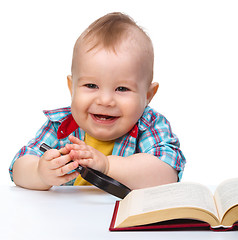 Image showing Little child play with book and magnifier