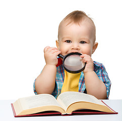 Image showing Little child play with book and magnifier