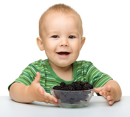 Image showing Cheerful little boy is eating blackberry