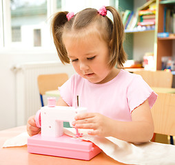 Image showing Little girl is playing with sewing machine