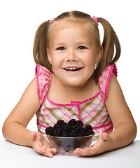 Image showing Cheerful little girl is eating blackberry