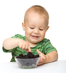 Image showing Cheerful little boy is eating blackberry