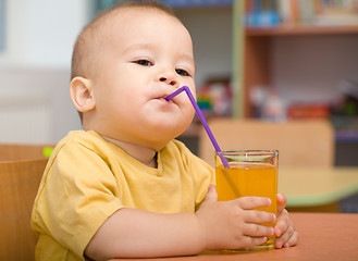 Image showing Little boy is drinking orange juice
