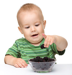 Image showing Cheerful little boy is eating blackberry