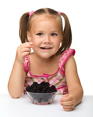 Image showing Cheerful little girl is eating blackberry