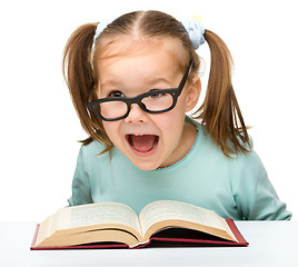 Image showing Little girl reads a book while wearing glasses