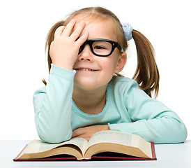 Image showing Little girl reads a book while wearing glasses