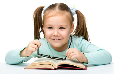 Image showing Little girl reads a book while wearing glasses