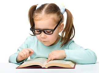 Image showing Little girl reads a book while wearing glasses