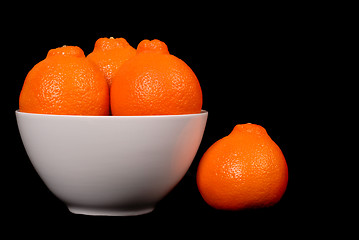 Image showing Three minneola oranges in white bowl with one orange at side