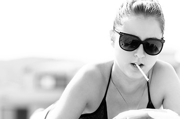 Image showing Young woman in swimsuit starting to smoke on the beach