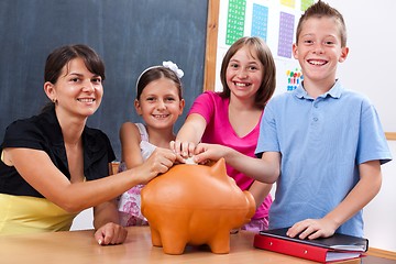 Image showing Students and teacher putting coin into piggy bank