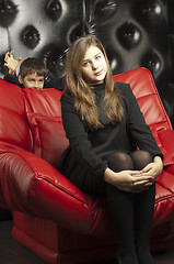 Image showing Young girl on a red leather sofa. Angry boy is coming fight