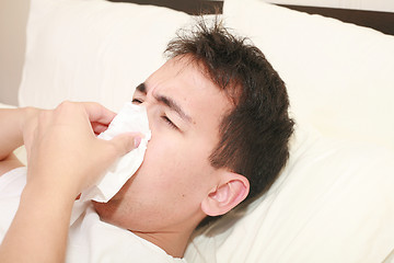 Image showing Sick man blowing his nose lying on his bed at morning