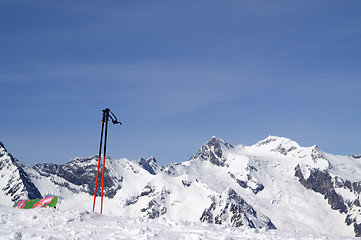 Image showing Ski poles and snowboard against snowy mountains