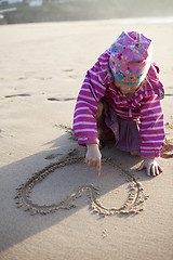 Image showing Girl drawing a heart in sand