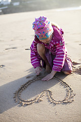 Image showing Girl drawing a heart in sand