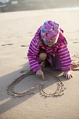 Image showing Girl drawing a heart in sand