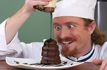 Image showing Funny young chef added chocolate sauce at piece of cake